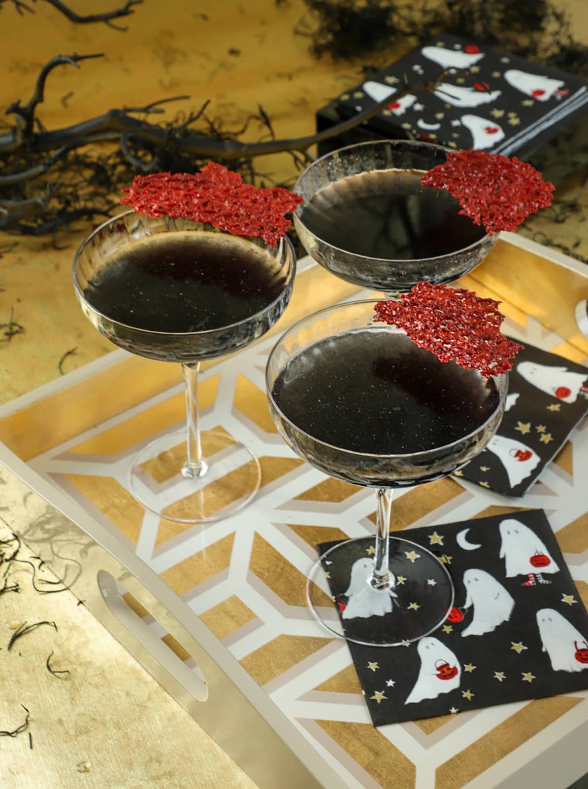 Ein Halloween dekorierter Tisch mit einem Tablett, auf dem schwarz-rote Cocktails stehen sowie die Caspari Servietten mit Geister-Motiv. Die weißen Gespenster sind mit Sternen auf einer schwarzen Serviette abgebildet.