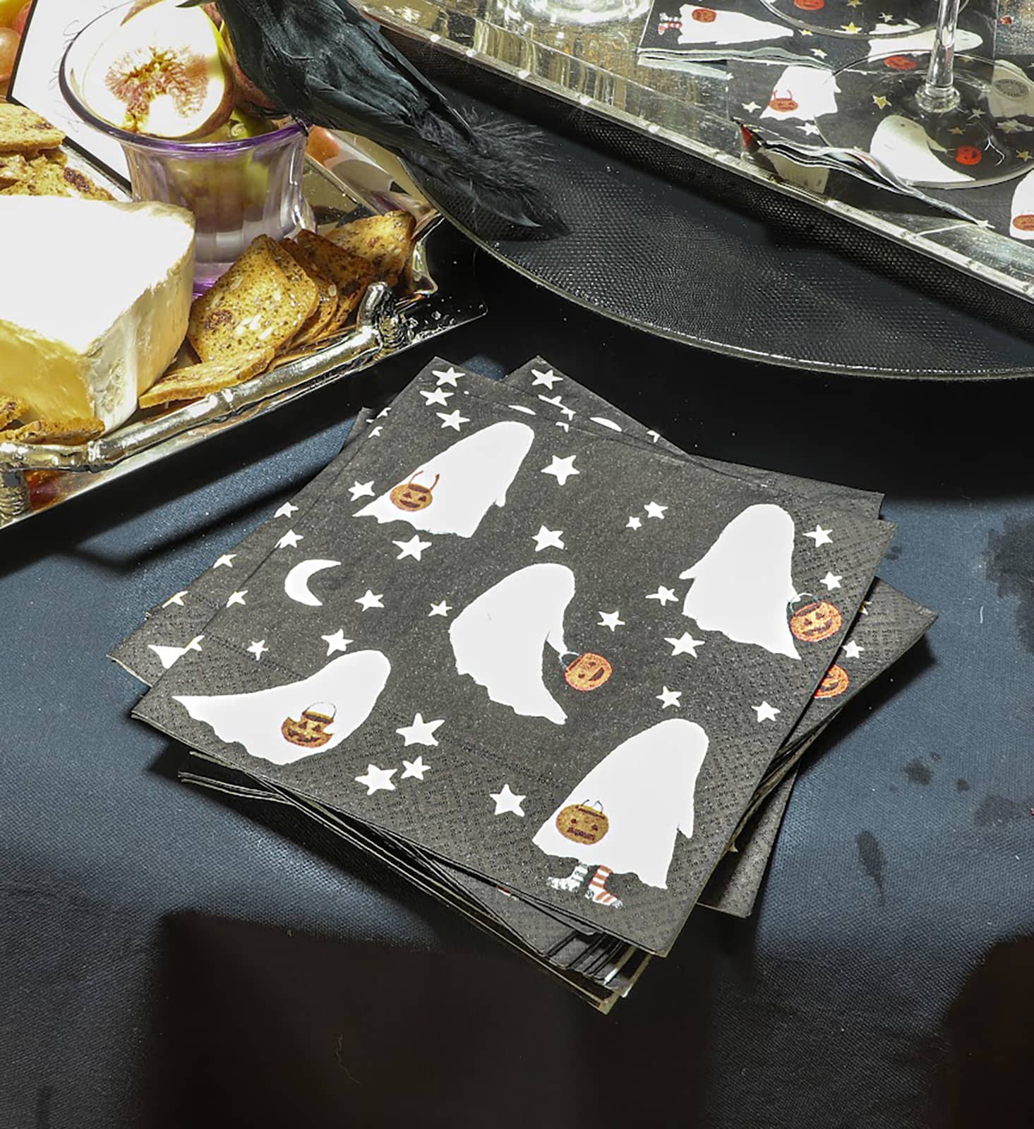 Ein Halloween dekorierter Tisch, in dessen Mittelpunkt die Caspari Servietten mit Geister-Motiv liegen. Die weißen Gespenster sind mit Sternen auf einer schwarzen Serviette abgebildet.